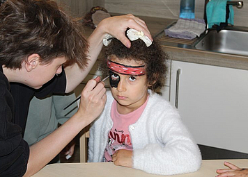 Ein Erzieherin schminkt das Kind mit einem Pinsel zum Piarten