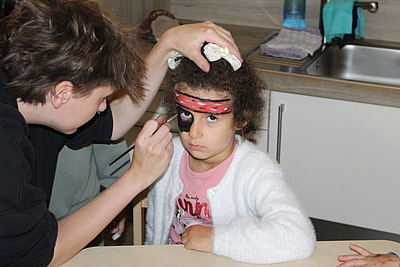Ein Erzieherin schminkt das Kind mit einem Pinsel zum Piarten