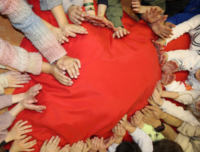 Eine Gruppe Kinder bildet mir ihren Händen einen Kreis auf einer roten Matte.