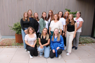 Auf dem Bild sind 13 verschieden alte Frauen zu sehen. Alle lachen und posieren für ein Gruppenbild.