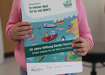 Wir sehen ein Wimmelbuch von der Stiftung Kinder forschen. Das Buch wird von einem Kind in den Händen gehalten.