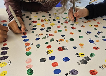 Eine Leinwand mit kleinen bunten Figuren, die unterschiedliche Gefühle zeigen. Am Rand Kinderhände, die an dem Bild arbeiten.