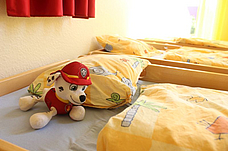 Zwei bezogene Betten aus dem Schlafraum. Auf dem Bett liegt ein Kuscheltier.
