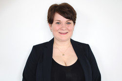 Eine lächelnde junge Frau mit kurzen dunklen Haaren vor einer weißen Wand. Sie trägt ein schwarzes Oberteil.