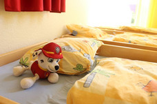 Zwei bezogene Betten aus dem Schlafraum. Auf dem Bett liegt ein Kuscheltier.