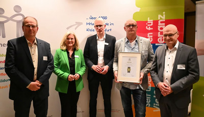 Vier Männer und eine Frau stehen mit der Urkunde der Wegbereiter-Veranstaltung vor einer bunten Rückwand.