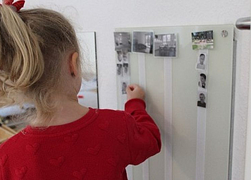 Ein Mädchen hängt ein Foto an einem Raumplan auf