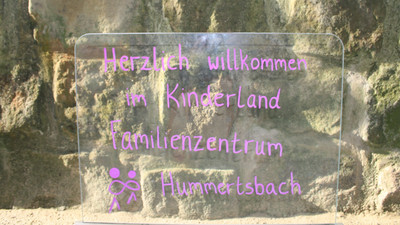 Dort steht ein Schild mit der Aufschrift "Herzlich willkommen im Kinderland Familienzentrum Hummertsbach".