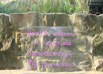 Dort steht ein Schild mit der Aufschrift "Herzlich willkommen im Kinderland Familienzentrum Hummertsbach".