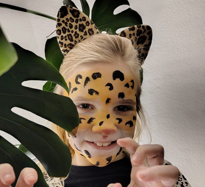 Gesicht eines geschminkten Mädchens als Leopard hinter Pflanze