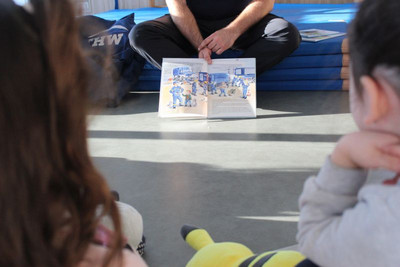 In der Mitte ist ein Buch und man sieht zwei Kinder, die beim Vorlesen zuhören