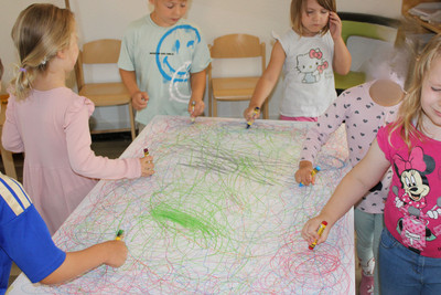 Sechs Kinder stehen mit geschlossenen Augen um einen Tisch und malen.