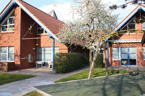 Die Kinderland-Einrichtung besteht aus drei Gebäuden. Der Spielplatz ist der zentrale Treffpunkt. Auf der rechten Seite steht eine Schaukel. Außerdem ist ein Birnenbaum zu sehen. Er ist nur einer der vielen Obstbäume der Kita.
