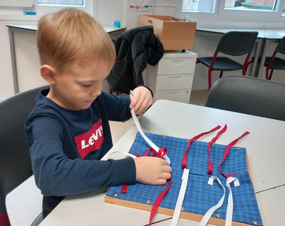 Auf dem Tisch liegt ein Schleifen-Rahmen. Ein Kind arbeitet an dem Schleifen-Rahmen.