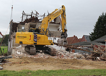 Auf dem Bild ist ein Bagger zu erkennen, der ein Haus abreißt.