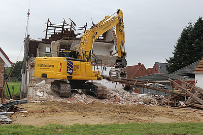 Auf dem Bild ist ein Bagger zu erkennen, der ein Haus abreißt.