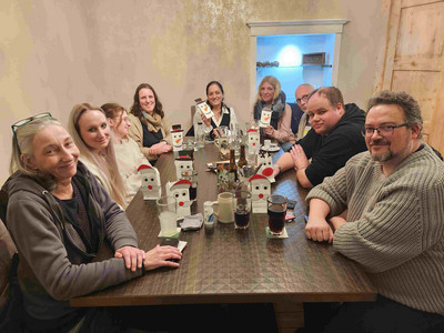 Ein Gruppenfoto. Zu beiden Seiten des Tisches sitzen Menschen, Getränke auf dem Tisch.