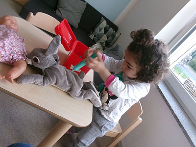 Ein Kind an einem Tisch auf dem Kuscheltierhase liegt un mit einer Spielzeug spritze in der Hand verarztet wird
