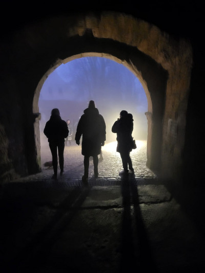 Drei Menschen im Schatten in einem Torbogen in Dunkelheit.