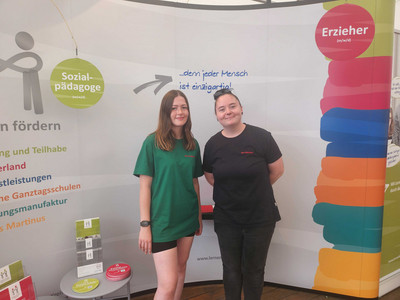Zwei Frauen vom Kinderland-Messeteam vor einer bunten Rückwand.