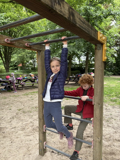 Zwei Kinder spielen auf einem Klettergerüst. Im Hintegrund sind Picknickplätze zu sehen. 