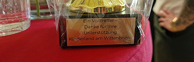 Der Sockel eines Pokals, dessen Aufstricht "Ein Volltreffer - Danke für Ihre Unterstützung Kinderland am Wittenbrink" lautet.