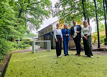 Vier Personen stehen auf einem Kunstrasenplatz im Außenbereich eines Kindergartens. 