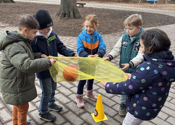 Fünf Kinder halten ein großes Tuch und balancieren einen Ball darauf.