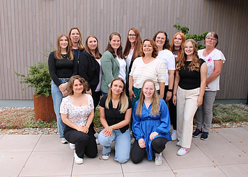 Auf dem Bild sind 13 verschieden alte Frauen zu sehen. Alle lachen und posieren für ein Gruppenbild.