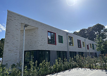 Auf dem Bild sieht man die Kinderland Einrichtung, ein beiges Gebäude mit bunten Fensterlaibungen. 