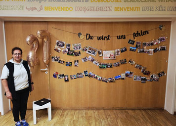 Eine Erzieher steht vor einer Wand mit schönen Fotos und einer Abschiedsgirlande.