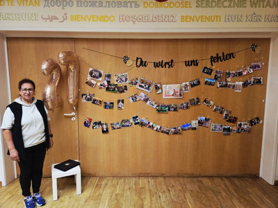 Eine Erzieher steht vor einer Wand mit schönen Fotos und einer Abschiedsgirlande.