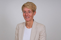 Frau mit Brille, kurzen blonden Haaren und Blazer 