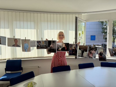 Eine Frau steht hinter einer Wäscheleine, an der ausgedruckte Fotos mit Wäscheklammern befestigt sind