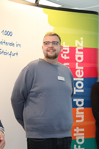 junger Mann mit grauen Pullover vor einer Werbewand