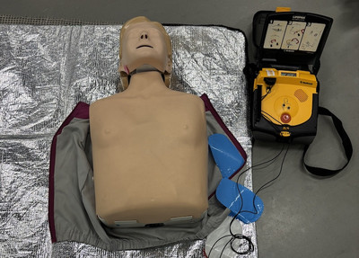 Demonstrationspuppe, Thorax liegt auf silberner Wärmedecke, rechts daneben ein Defibrillator 