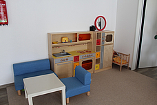 Eine Kinderküche. Die Küche steht hinten an der Wand und der Tisch mit den Sesseln steht links daneben