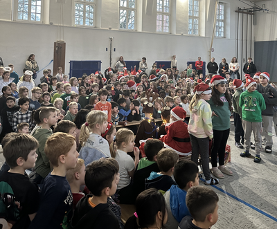 Ein Gruppenfoto in einer Kirche. Ein großer Chor bestehend aus vielen Kindern steht in mehreren Reihen hintereinander. Davor ein Mann verkleidet als Weihnachtsmann.
