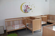 Ein heller Schlafraum, mit Gitterbtten und einem Wandtattoo darüber 