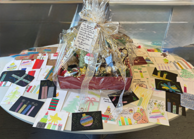 ovaler Tisch mit einem Geschenkkorb mit Plätzchen, Körnerkissen und weihnachtlichen Kleinigkeiten. Um den Korb liegen selbstgebastelte und geschriebene Weihnachtskarten.