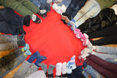 Eine Gruppe Kinder bildet mit ihren Füßen einen Kreis auf einer roten Matte am Boden.