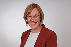 Frau mit Brille und kurzen hellbraunen Haaren und braunem Blazer