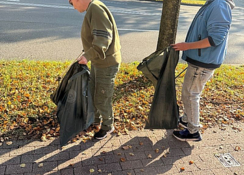 Zwei Personen sammeln Straßenmüll vom Gehweg