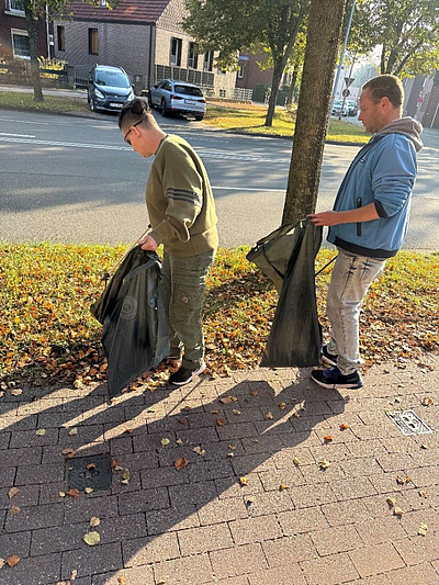 Zwei Personen sammeln Straßenmüll vom Gehweg
