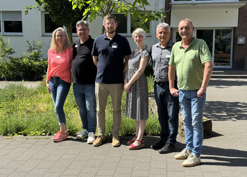 die 5 Personen, die bei dem Treffen dabei waren, stehen in einer Reihe draußen vor einem Gebäude