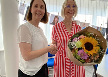 Zwei Frauen geben sich die Hände, eine davon hält einen Blumenstrauß
