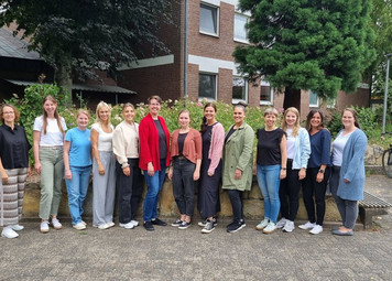 13 Frauen stehen nebeneinander für das Foto an einer Mauer, ein Seminargebäude im Hintergrund