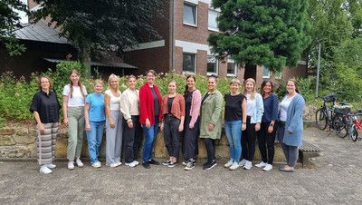 13 Frauen stehen nebeneinander für das Foto an einer Mauer, ein Seminargebäude im Hintergrund