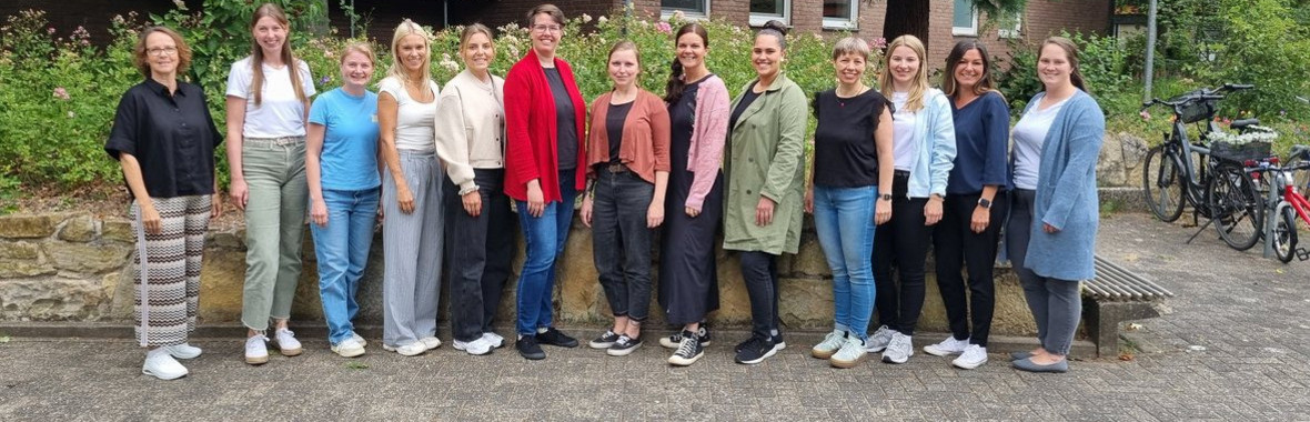 13 Frauen stehen nebeneinander für das Foto an einer Mauer, ein Seminargebäude im Hintergrund