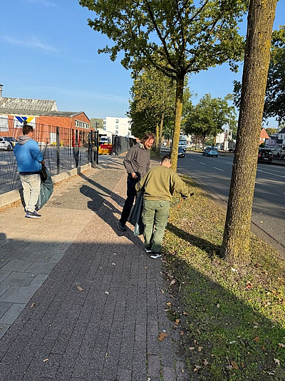 Drei Personen sammeln Straßenmüll vom Gehweg